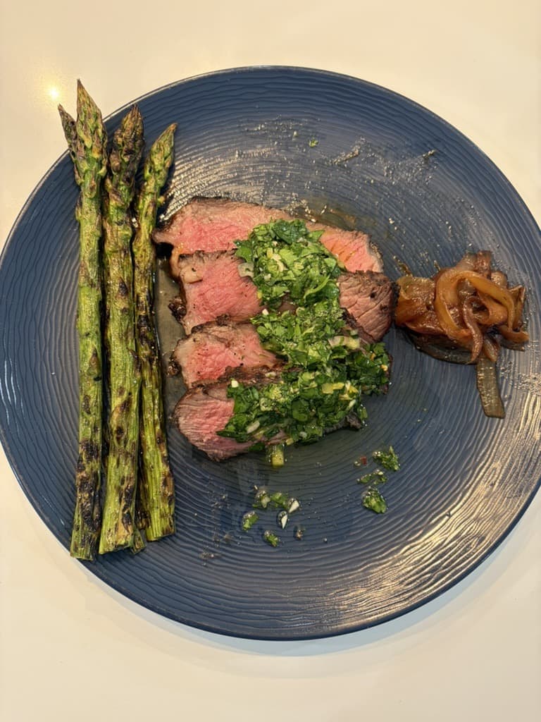 Sliced steak with chimichurri, grilled asparagus, and caramelized onions