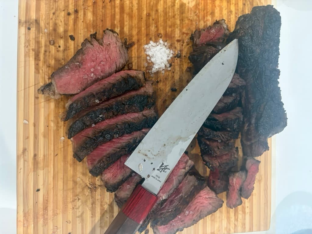 Sliced medium-rare steak on a cutting board with a chef knife